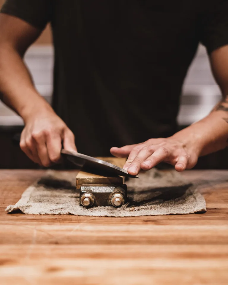 Hands sharpening a kitchen knife on a whetstone